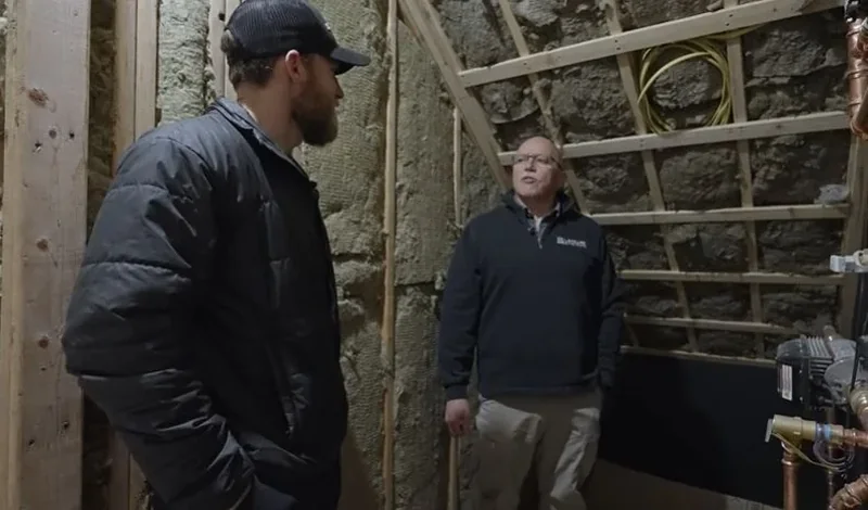 Plumber listening to a homeowner describe a plumbing problem in an unfinished basement