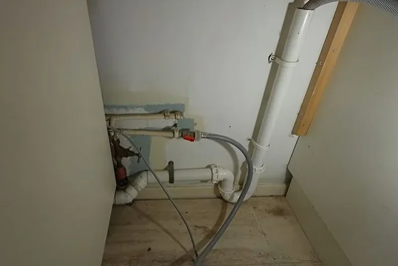 Laundry area wall with supply lines and a drain pipe behind the washing machine space
