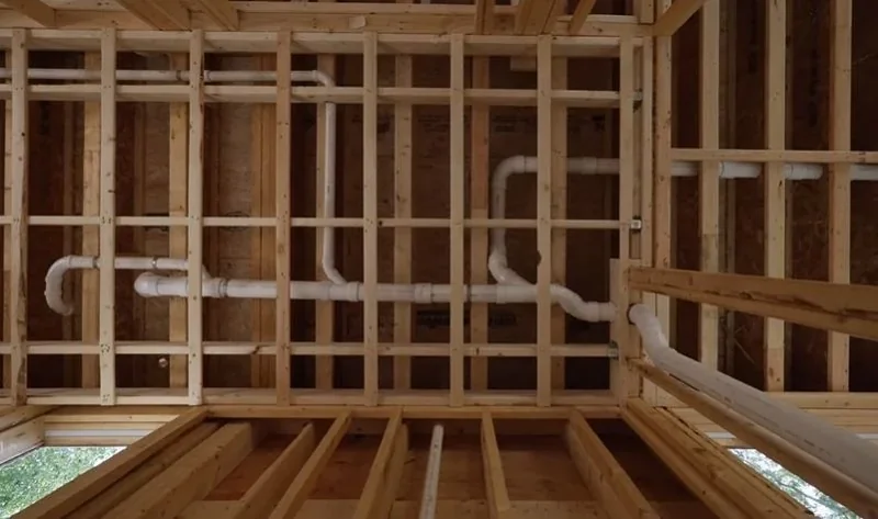 White PVC drain lines running through floor joists under a kitchen