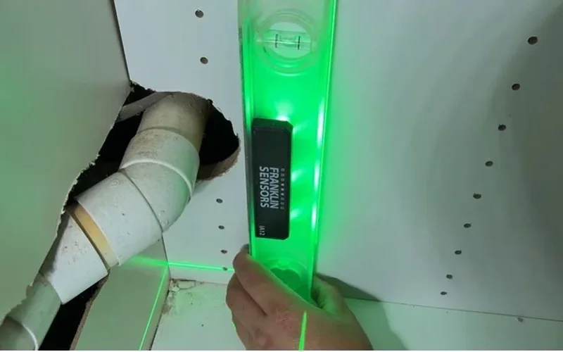 Plumber checking the slope of a PVC drain line with a digital level
